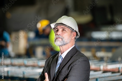 older owner engineer with beard mustache on face standing smile with his arms crossed at construction factory site. Boss manager in suit show good thumb at factory industry site.