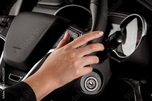 Young woman's hand driving a new car holding the leather steering wheel inside the new vehicle - close up driving test