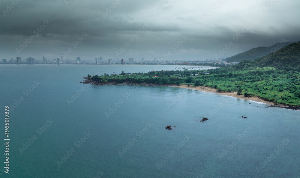 Fototapeta premium An aerial view of Da Nang, Vietnam, showcasing the city's coastline and skyline on a cloudy day. The image captures the blend of urban and natural landscapes.