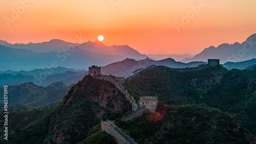 Jinshanling section of the Great Wall of China at sunset, with the ancient wall winding across mountain ridges under a glowing sky. 