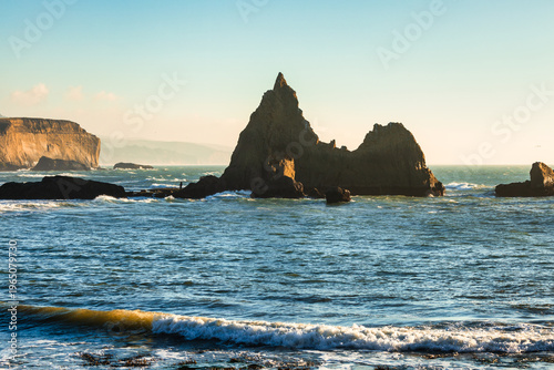 Dramatic sea stacks and rugged rock formations at Martins Beach on the California coast, with ocean waves, warm sunset light, and colorful sky over the Pacific Ocean