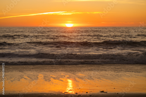 Warm ocean sunset with the sun touching the horizon, gentle waves rolling toward the shore, golden sky reflecting on the water, creating a peaceful and atmospheric seascape with calm mood