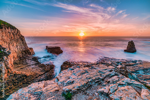 A sea stack rises from the Pacific Ocean at Davenport Beach, California, as soft waves and warm sunset light reflect on wet sand, creating a calm and scenic coastal view