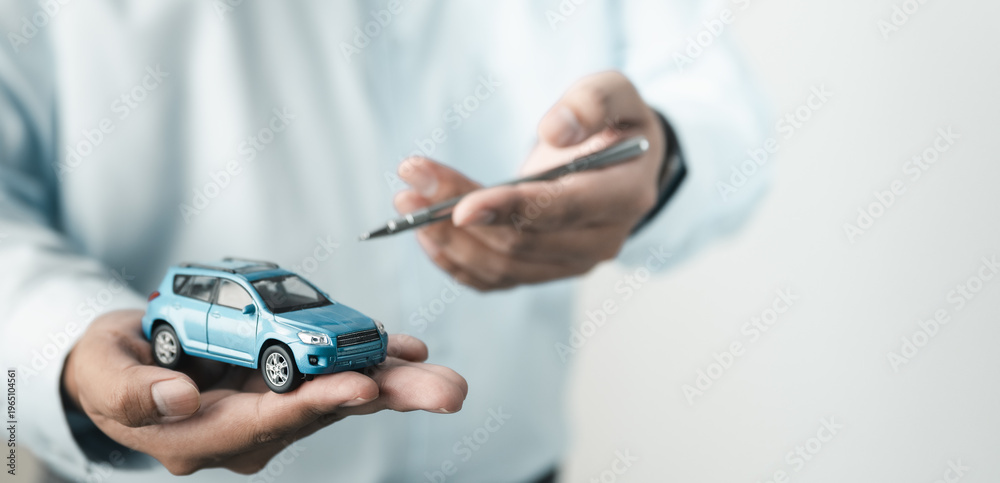 Fototapeta premium Person holding car model while signing agreement, representing vehicle purchase, auto loan, insurance policy and dealership contract process.