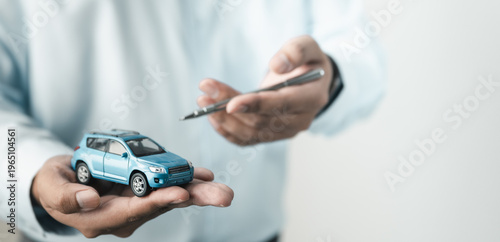 Person holding car model while signing agreement, representing vehicle purchase, auto loan, insurance policy and dealership contract process.