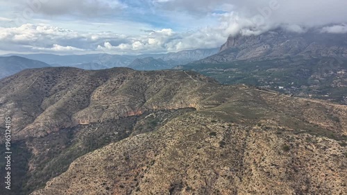 Aerial arid ridge over scrub and rocky hills, geological survey perspective, cloud shadows on brown slopes