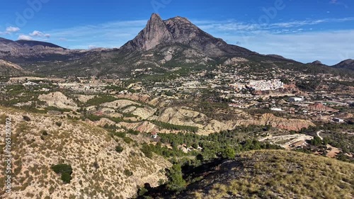 Sunlit monolith mountain above town and terraced fields, bright blue sky, sweeping valley views, agricultural