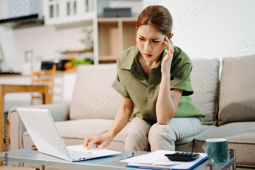 Financial stress and debt management. Worried Asian woman analyzing domestic bills and expenses with laptop and calculator in her home living room.