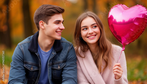 A guy and a girl are sitting in a park, smiling, and the girl is holding a balloon on a string.	
