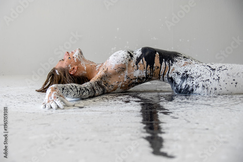 Person lying on studio floor covered with black and white paint creating strong contrast, abstract textures and expressive artistic composition with dynamic visual impact