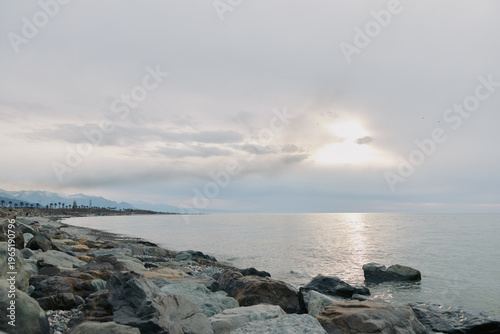 Принти на полотні Rocky shoreline under cloudy sky at calm sea during sunset