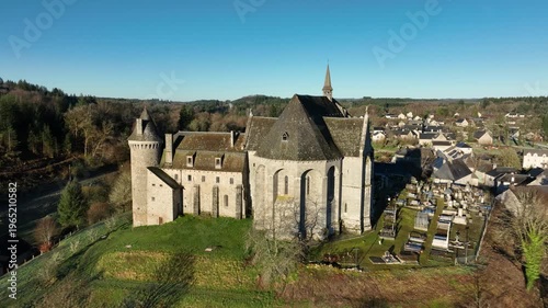 Aerial view of historic Saint Angel romanesque church with conical tower and spire overlooking village cemetery and rural landscape in Correze France under clear blue sky