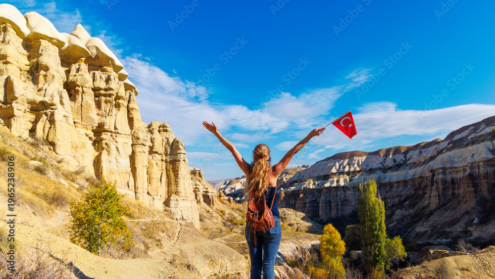 Obraz premium Young Woman Hiker Celebrating with Turkish Flag Overlooking Cappadocia Fairy Chimneys Landscape