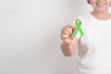 Elderly with light Green Ribbon for concept of May Celiac Awareness month, Lyme disease, September Lymphoma, Mental Health Awareness month and October Liver cancer. Health and world cancer day