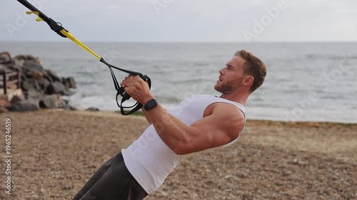 Side profile view young strong sporty athletic fit sportsman man he wear sports clothes use trx loops pull up warm up train at sunrise sun over sea beach outdoor on pier seaside in summer day morning