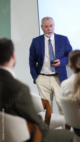 Senior man lecturer with remote controller speaks to business audience of listeners, shares knowledge, communicates with listeners. Speaker reports on changes in companys policy provisions. 