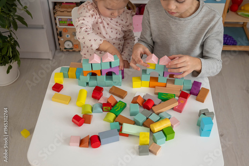 Brother and sister playing with colorful wooden building blocks at home