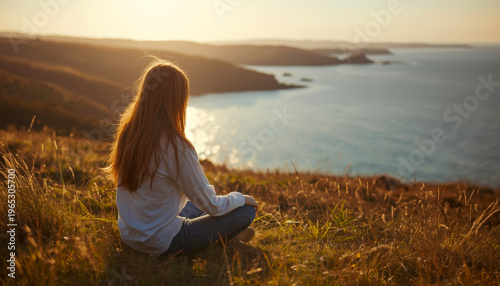 Back view of a person meditating outdoors on a hill in front of the sea, a calm peaceful environment