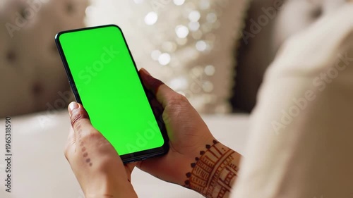 delicate female hands in a light t-shirt gently cradle a black smartphone with a glowing green screen mockup. cozy home living room, soft natural light, slow micro-dolly zoom out, creamy bokeh.