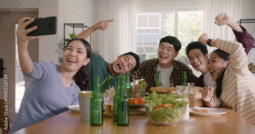 Happy hour diner at home relax smile look at camera shooting video photo on mobile app. Group of asia people young adult friend man and woman sit at dining table joy fun talk or eat food drink beer.