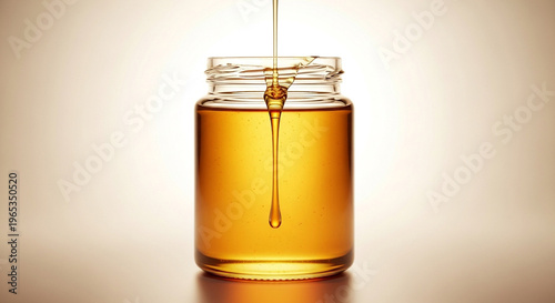 Pure Golden Honey Pouring into a Clear Glass Jar on Minimalist Background