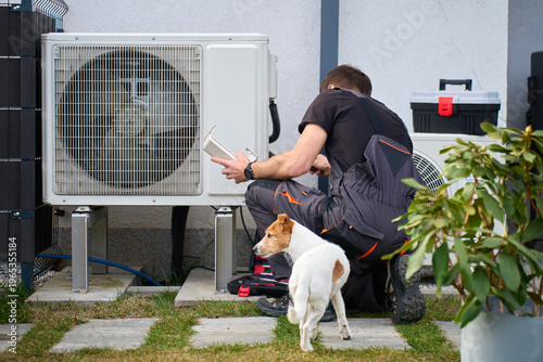 Принти на полотні Technician servicing outdoor heat pump unit near residential building with dog nearby