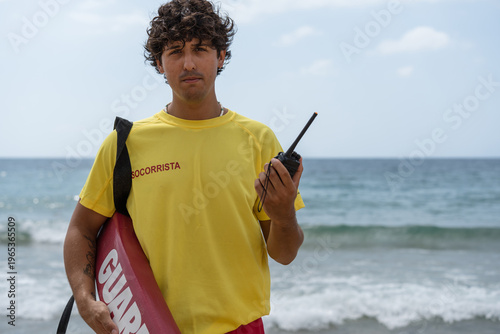 Fotografie Lifeguard holding rescue board and walkie-talkie on beach