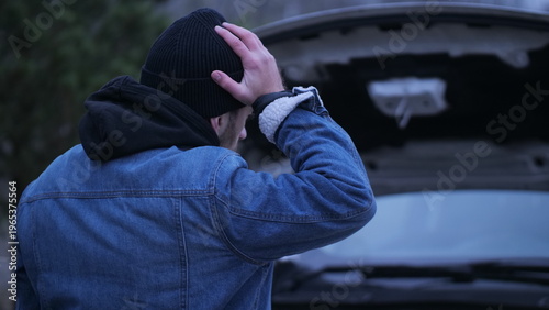 Bild auf Leinwand Man stands by broken down car with hood open, hand on head, staring at engine in