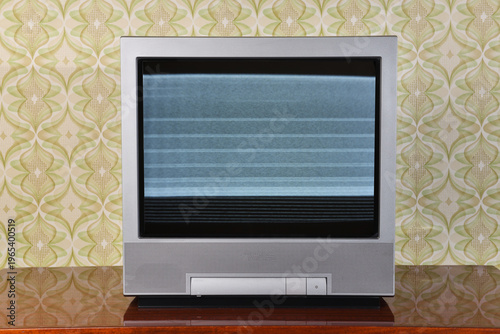 Old silver CRT TV with static on the screen against vintage wallpaper background.