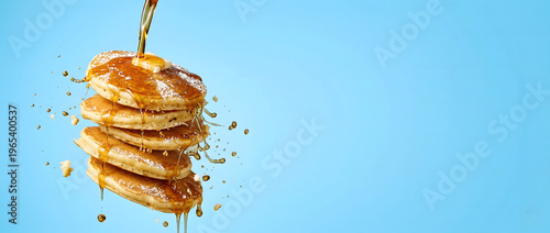 Falling stack of pancakes with syrup pouring on light-blue background with copy space