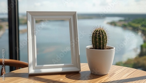 A serene scene featuring a white picture frame and a small potted cactus on a wooden table overlooking a tranquil body of water.