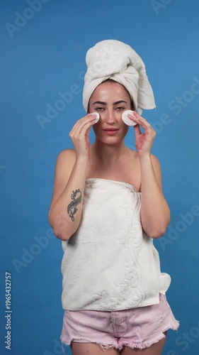 Woman with a towel turban removing makeup with cotton pads