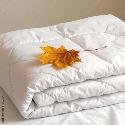 A neatly folded white comforter with a yellow leaf on top