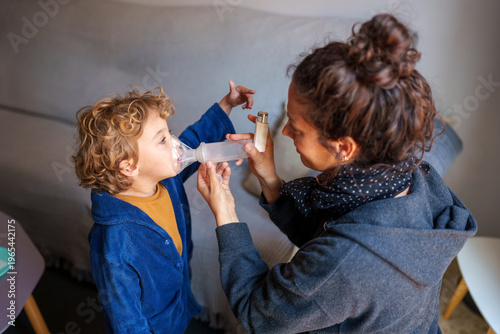 Fotografia Mother helping her young child to take asthma medication using an inhaler and sp