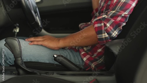 A man wearing a red plaid shirt is fastening his seatbelt in his private car. This is a safety precaution before driving.
      man, wearing, red, plaid, 