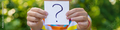 The child holds a paper with a question mark. Selective focus.