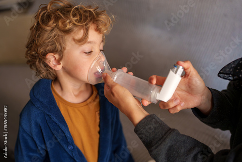 Quadro em tela Child with curly hair receiving breathing treatment via an asthma inhaler and sp