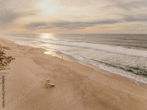Aerial view of a lone lifeguard chair sits on the expansive sandy beach meeting the rhythmic waves under a muted sky, Quiaios Beach, Figueira da Foz, Portugal.