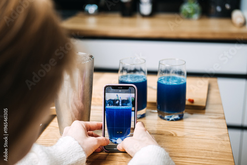 Person uses smartphone to photograph blue drinks being garnished by bartender on wooden table. Interactive Mixology Workshops, cocktail masterclass, content creation, culinary education.