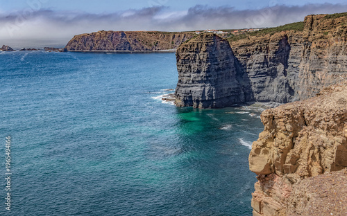 view on a big rock on the high cliffs at edge of the clear sea in coast in Portugal in the Algarve under blue sky sky
