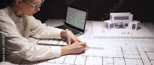 Photos Adult female architect intensely working at a desk with blueprints, cad on lapto