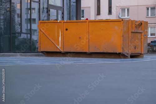 Orange construction waste container near residential building, urban renovation concept
