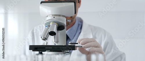Scientific researcher wearing lab coat, glasses and white protective gloves carefully calibrating laboratory microscope, performing precision medical investigation. Medicine, healthcare and science