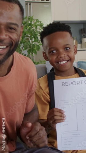 Vertical video: Celebrating dad clapping, pumping after son showing REPORT on couch, with coral tee