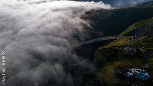 Aerial view of wispy clouds dance with the rolling green hills, as sunlight catches the roofs of houses along Via Acero, Malibu, California, United States.