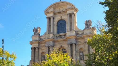View of the Saint-Gervais-Saint-Protais church facade framed by the green leaves of a tree in the foreground at Place Saint-Gervais in Paris, France