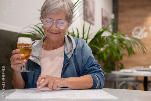 Smiling senior woman sitting at restaurant table while choosing what to eat from menu