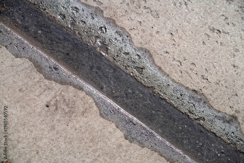 Narrow water channel formed by melting snow running between concrete plates. Abstract urban texture with diagonal line, wet surface and construction material background. Photo