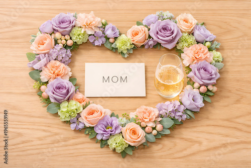 Top-down flat lay of a heart made of lavender, peach, and sage blooms on oak wood. A minimalist "MOM" card and a champagne flute sit inside the heart. Airy, high-key lighting. 16:9.