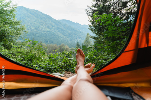 фотографія Bare feet resting inside an orange tent with a beautiful view of green mountain peaks